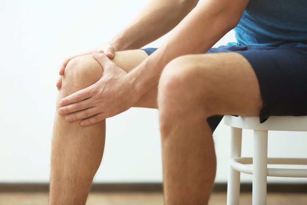Young man suffering from knee pain at home, closeup
