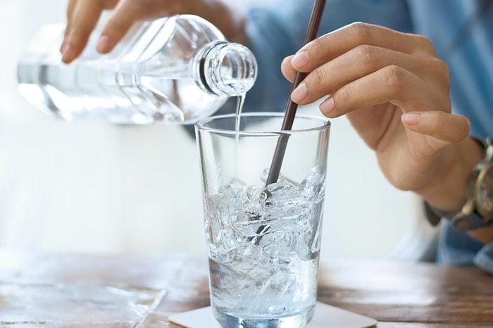 person pouring water into glass with ice and straw