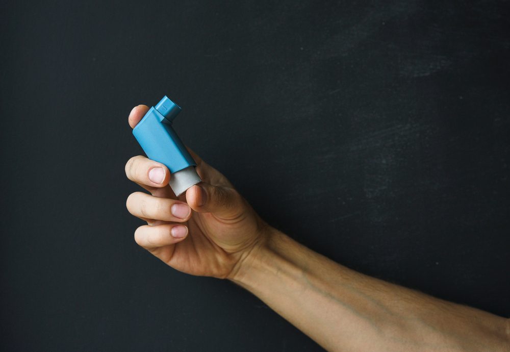 aerosol inhaler for the treatment of asthma in a male hand against a dark background.