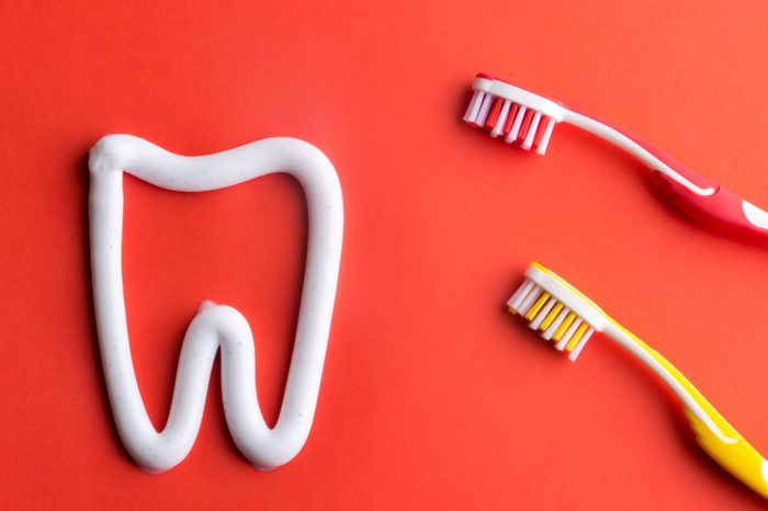 White toothpaste in a form of a tooth with red and yellow tooghbrushes on red background. White toothpaste and toothbrushes. Red and yellow tooghbrushes.