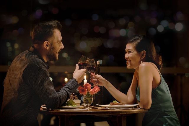 Cheerful couple clinking glasses at late romantic date in restaurant