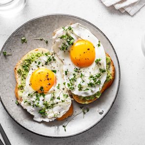 Metabolism boosting foods - Avocado Egg Sandwiches and coffee for healthy breakfast. Whole grain toasts with mashed avocado, fried eggs and organic microgreens on white table.