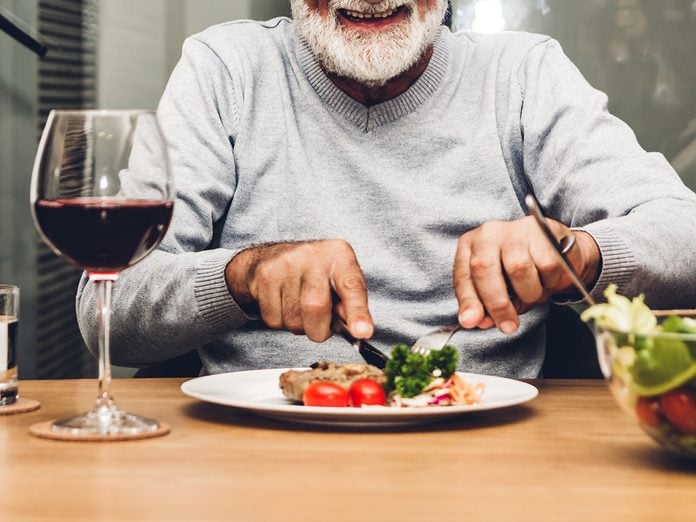 Happy senior man eating pork steak on table at restaurant