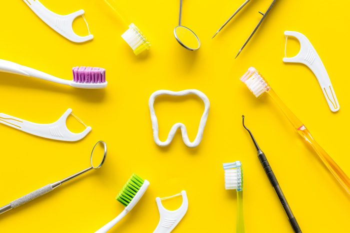 Oral hygiene concept. Tooth drawn with toothpaste near toothbrush, dental floss on yellow background top view