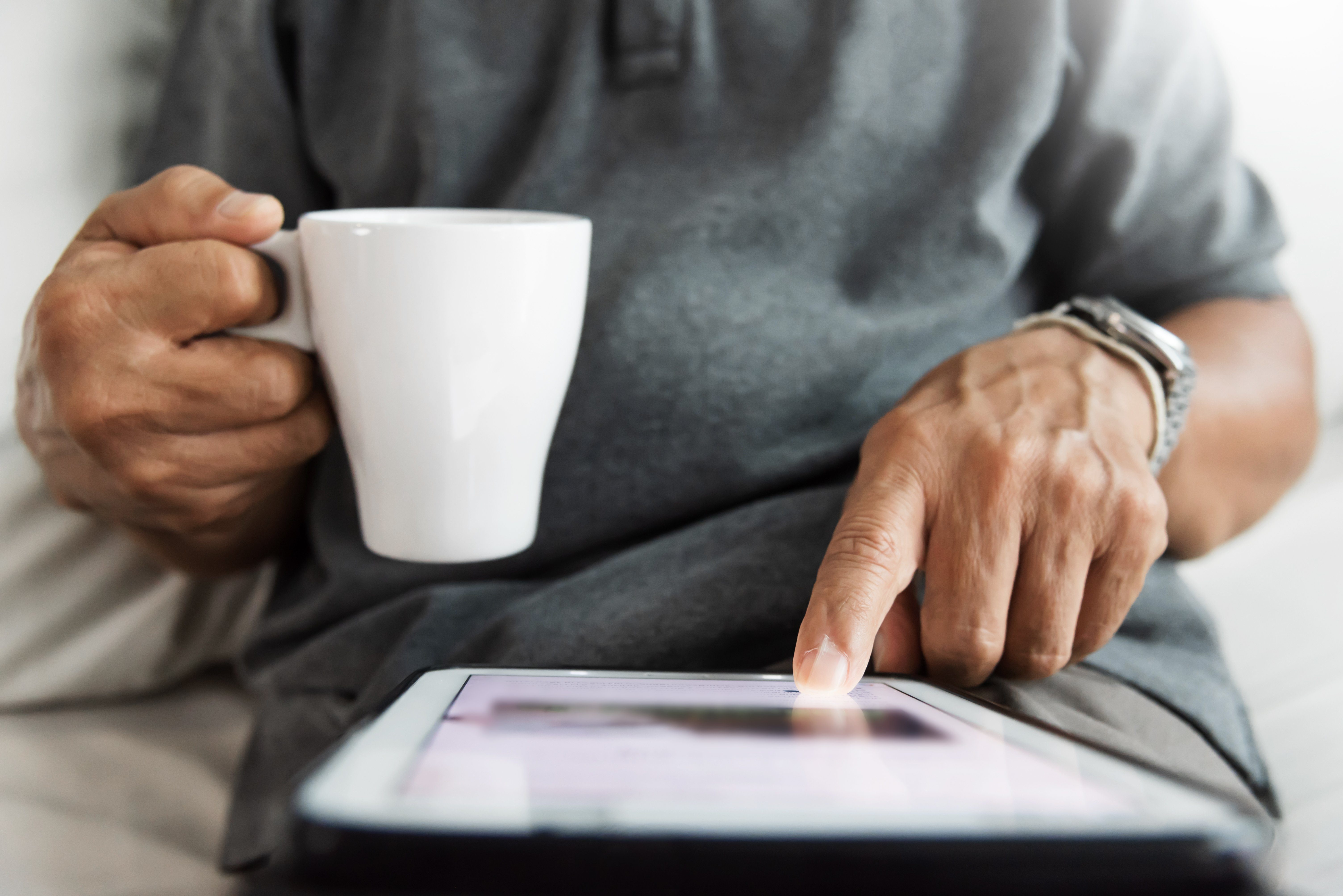 Close up Senior male hands using digital tablet. Happy Asian Man sitting on sofa and holding cup of coffee.