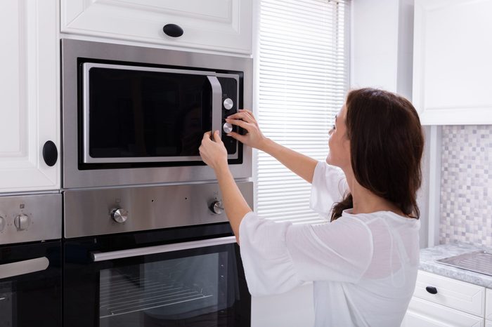 Side View Of A Young Woman Using Microwave Oven In Kitchen