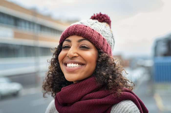 Closeup face of young happy woman enjoy winter, wearing scarf and woolen cap. Smiling black girl looking away outdoor. Carefree african american woman with knitted hat and woolen scarf outdoor.