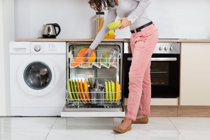 Woman Standing In Kitchen Removing Bowls From Dishwasher