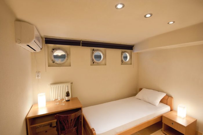 Boat deck with round windows, luxurious furnished cabin bedroom on a cruise ship, ceiling lights and wine on the desk 