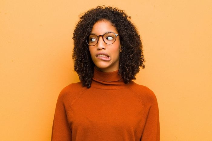 young pretty black woman feeling shocked, happy, amazed and surprised, looking to the side with open mouth against orange wall