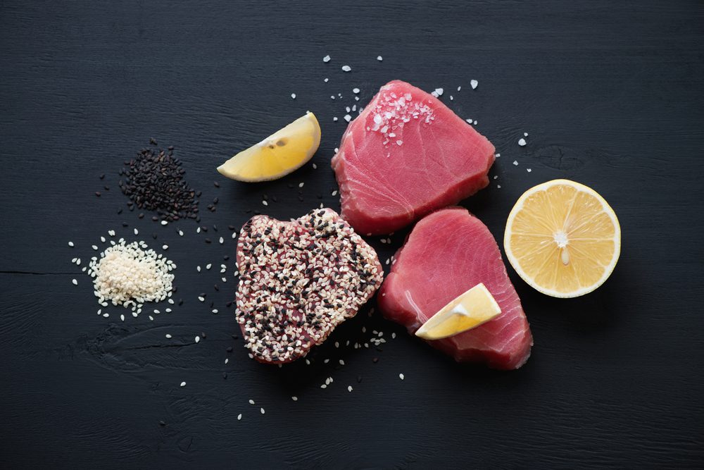 Raw tuna steaks with sesame, black wooden surface, flat-lay view