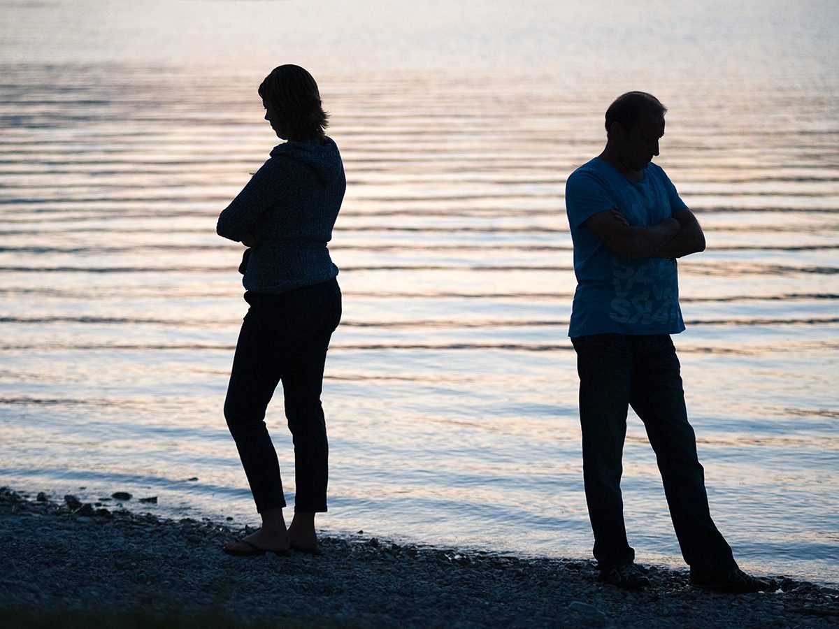 Things to Never Do After a Fight - Couple standing apart on the lake shore with arms crossed