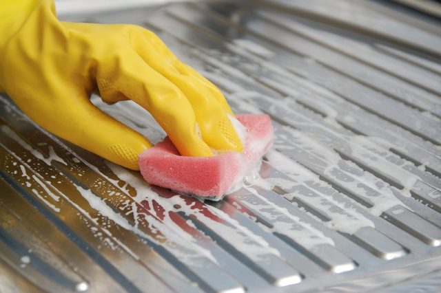 Cleaning Kitchen Sink with a Chemical Cleaning Solution. Housekepeeng, Yellow Gloves and Sponge.