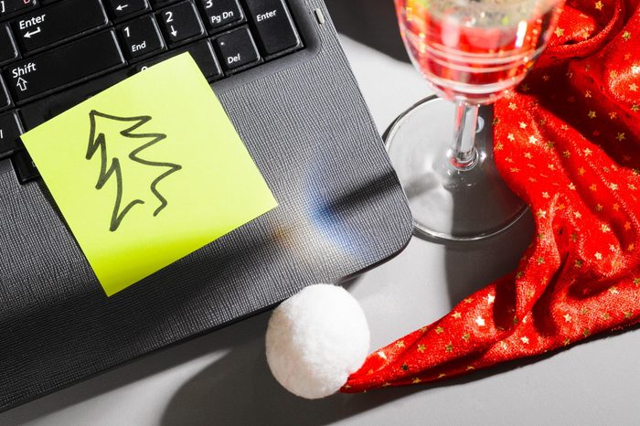 laptop with santa hat and sparkling wine and spruce on sticky note on gray