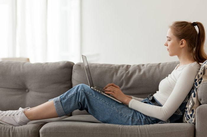 Relaxing woman using laptop in living room, working on online project, internet shopping, sitting on comfortable sofa, reading email, chatting in social network, looking at screen, typing
