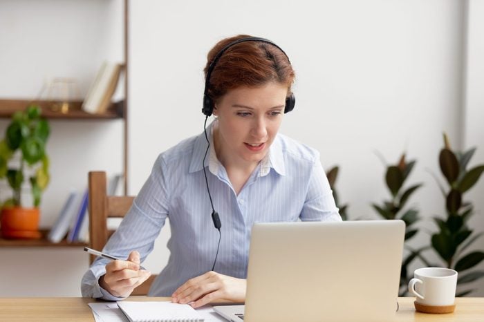 Businesswoman wearing headphones watching video webinar making conference online call writing notes talking, focused woman study online looking at laptop listening translating lecture course
