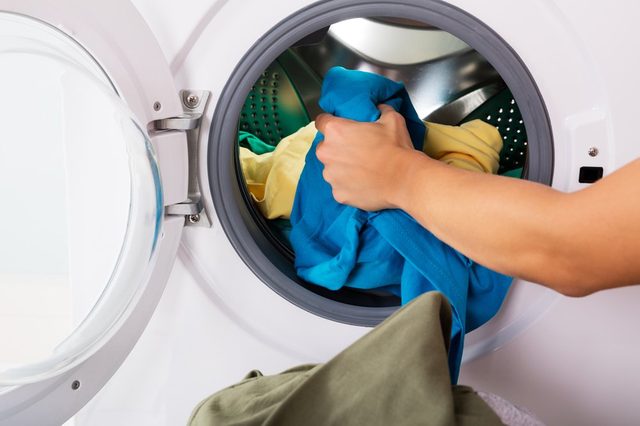 Close-up Of Woman Hand Loading Dirty Clothes In Washing Machine