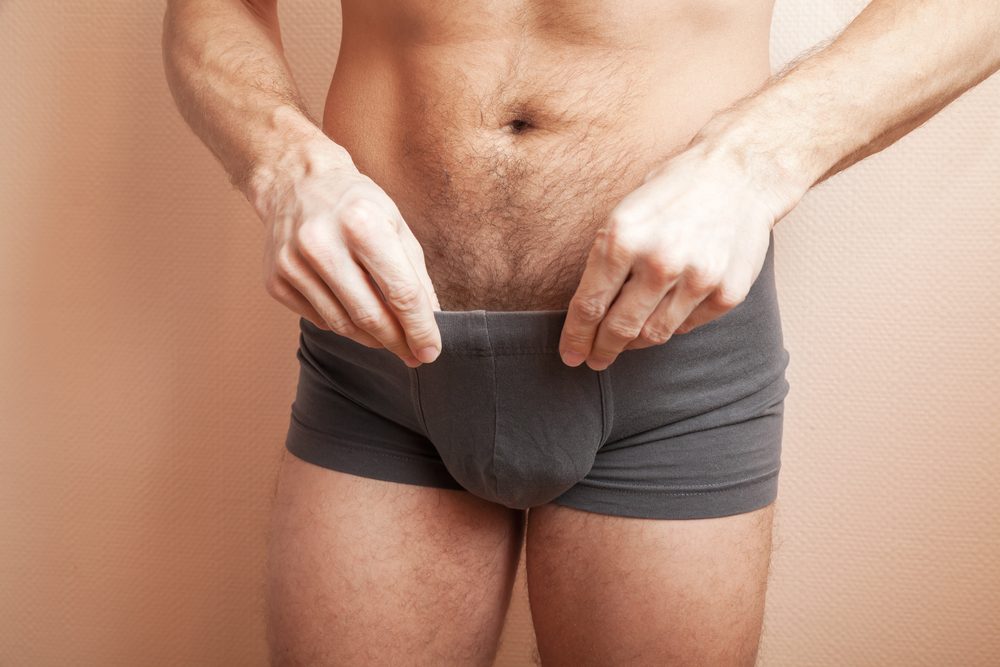 Young adult sporty man pulls out dark gray boxer underpants, close-up studio photo with selective focus