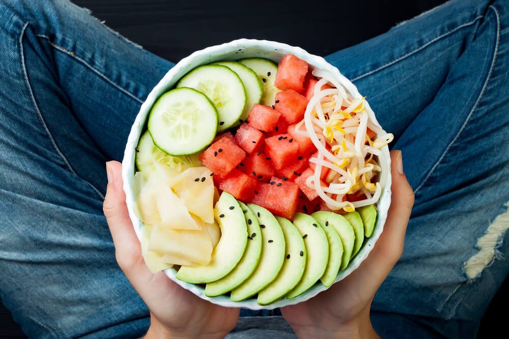 Girl in jeans holding hawaiian watermelon poke bowl with avocado, cucumber, mung bean sprouts and pickled ginger. Top view, overhead