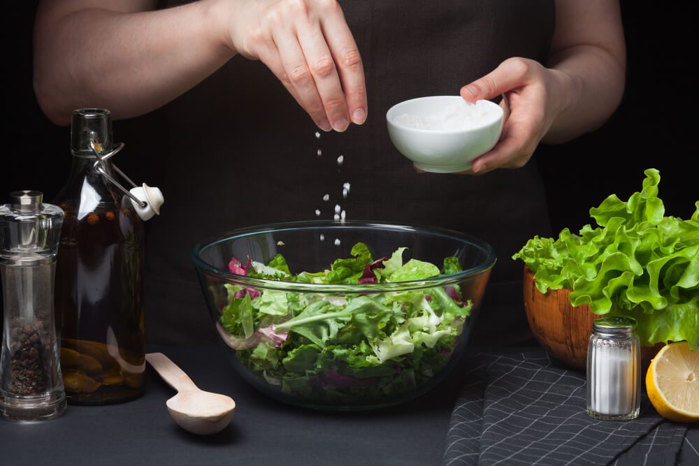 Woman chef in the kitchen preparing vegetable salad. Healthy Eating. Diet Concept. A Healthy Way Of Life. To Cook At Home. For Cooking. The girl sprinkles sea salt in a salad on a dark background