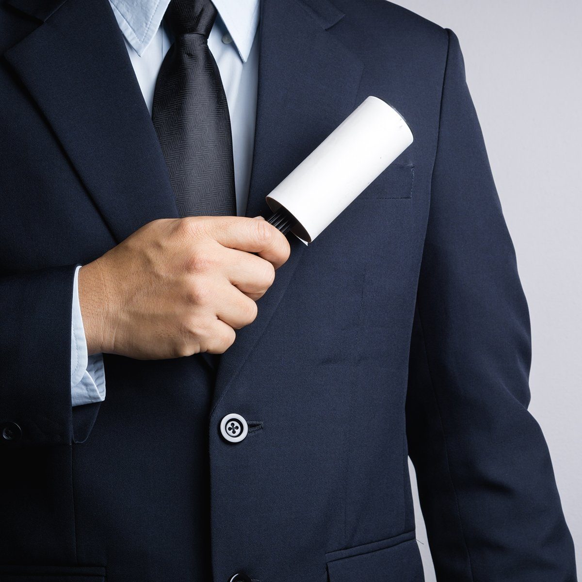 Business man cleaning his suit with adhesive lint roller on white background