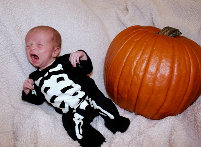 An infant in a skeleton costume crying next to a pumpkin