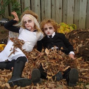 Two kids in zombie costumes in a pile of leaves