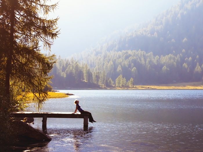 Woman seen from a distance sitting on a dock by a lake