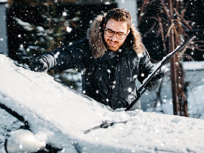 How to remove snow from car - man brushing snow off windshield