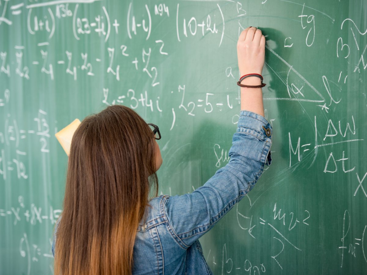 Schoolgirl with glasses writing on blackboard