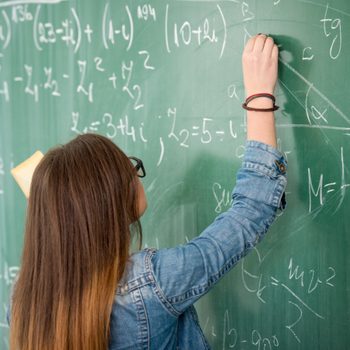 Schoolgirl with glasses writing on blackboard