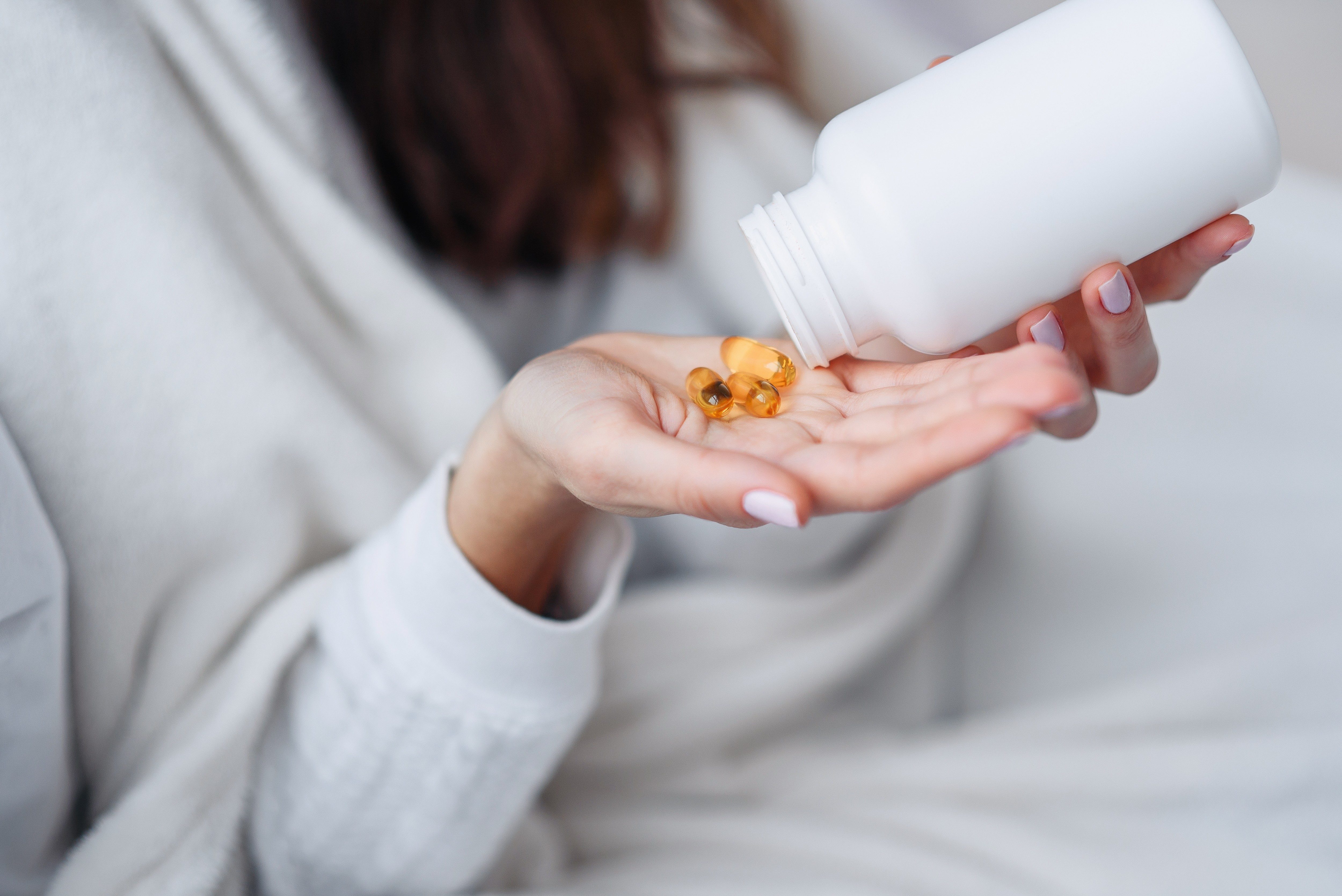 Vitamins and food supplements concept. Closeup of female hand pouring yellow pills out of bottle into palm. Woman spilling out medication, tablets, capsules on hand.