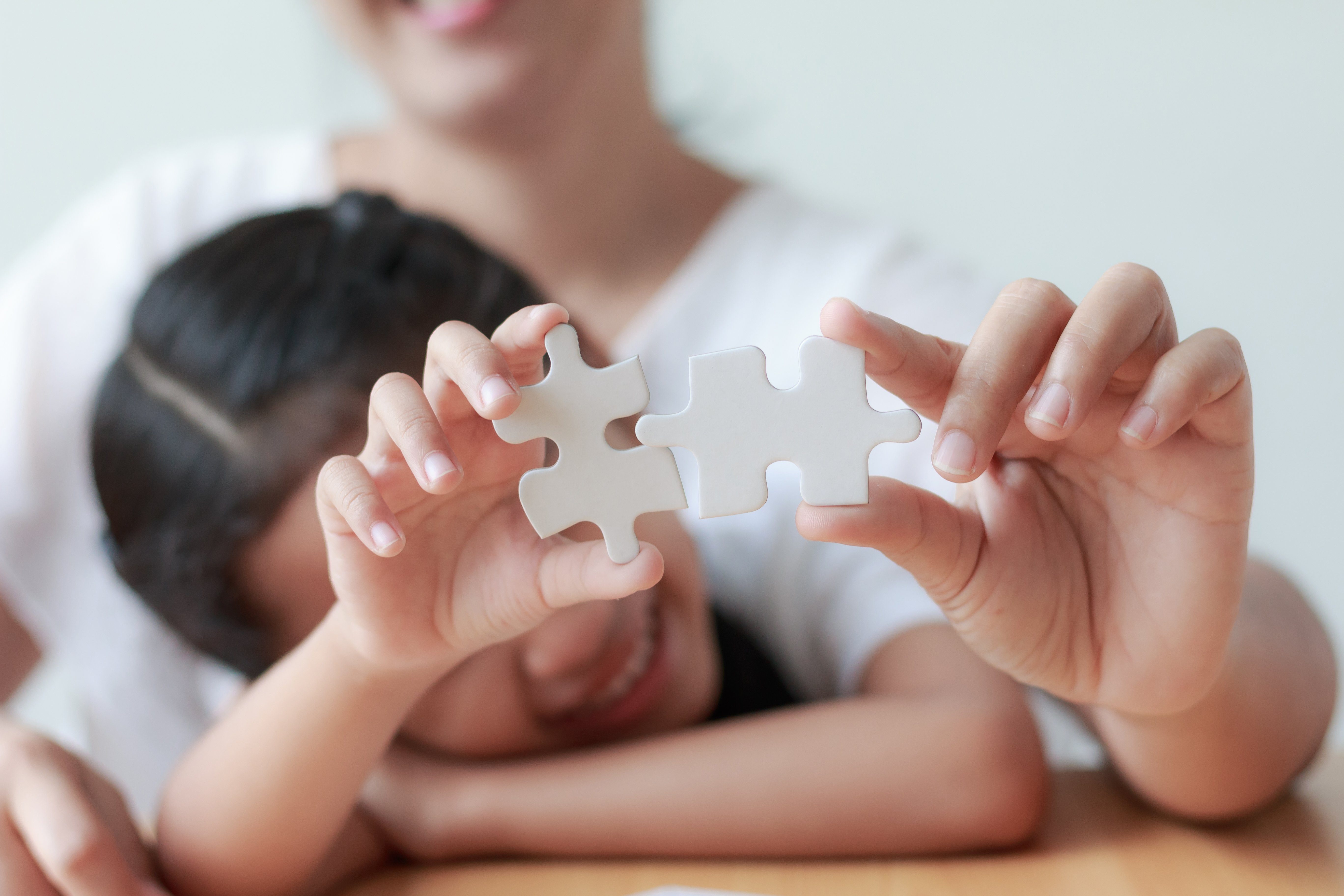 Asian little girl playing jigsaw puzzle with her mother for family concept shallow depth of field select focus on hands