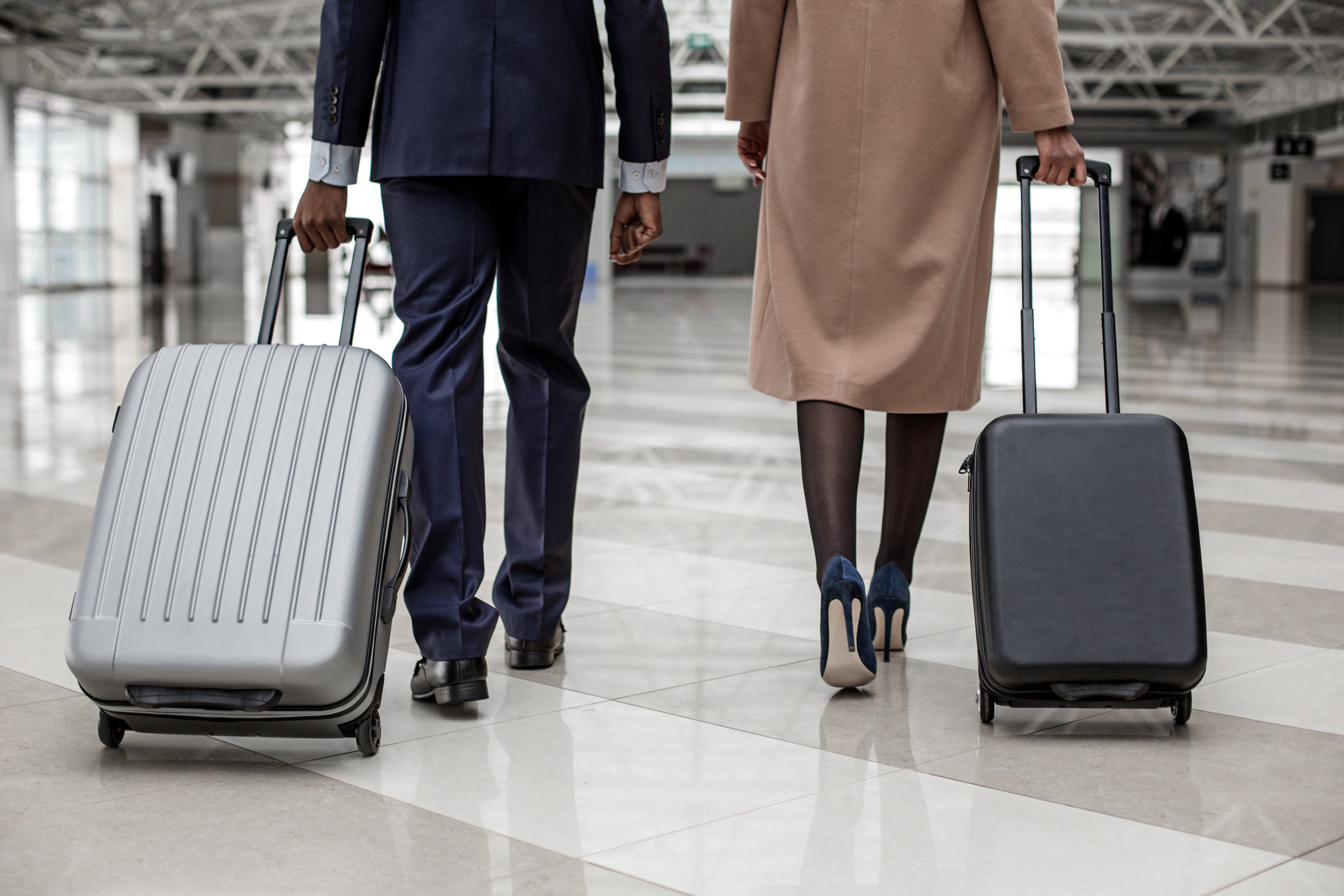 Close-up back view of legs of elegant businesswoman and businessman are going along terminal lounge. They are carrying their luggage to departure area