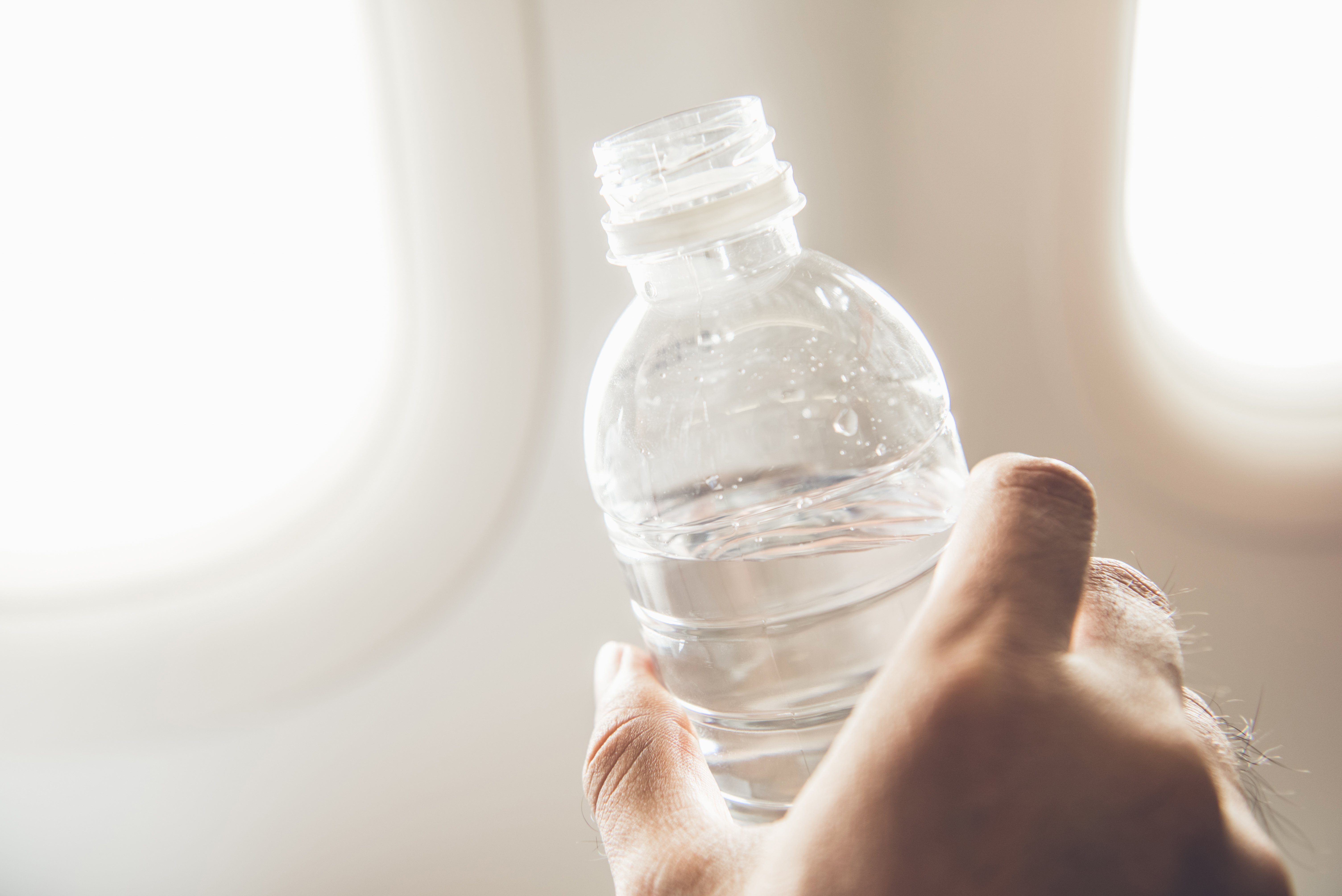 Passenger holding bottle of water about to drink preventing dehydration while traveling on the plane 