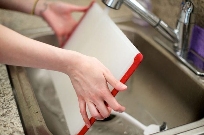 Woman washes cutting board in kitchen sink