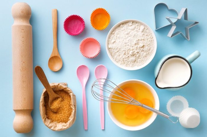 Baking utensils and ingredients. Egg yolk, brown sugar, milk, flour, whisker, spoons, cinnamon, bowl, rolling pin, cupcake paper cup, molds, sweet decoration elements. Top view. Flat lay