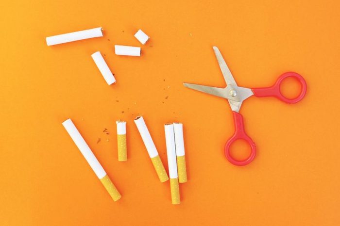 cut cigarettes and red scissors on orange background