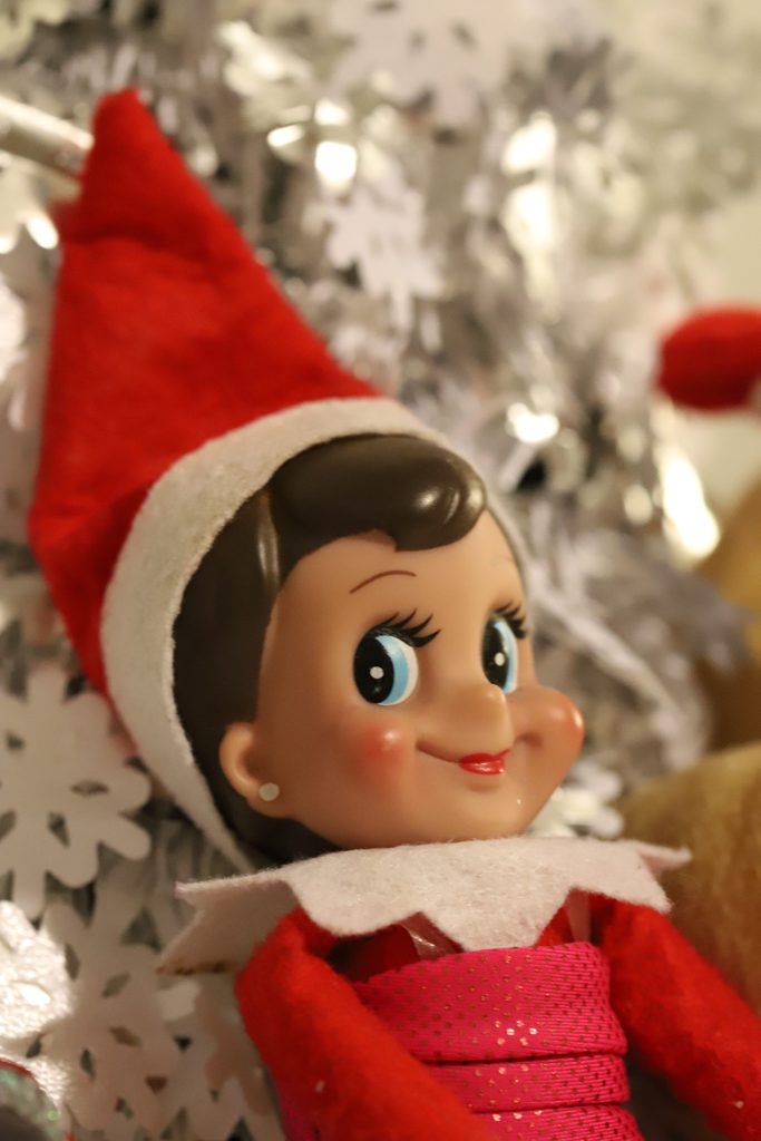 An elf on the shelf toy in front of a tree