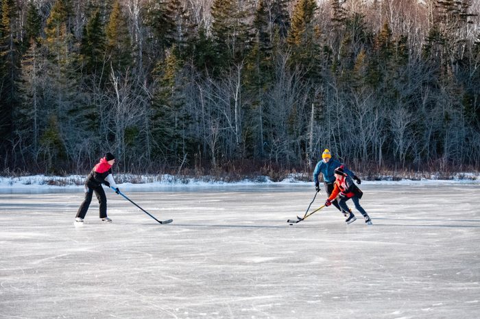Family playing shinny on outdoor rink in front of trees