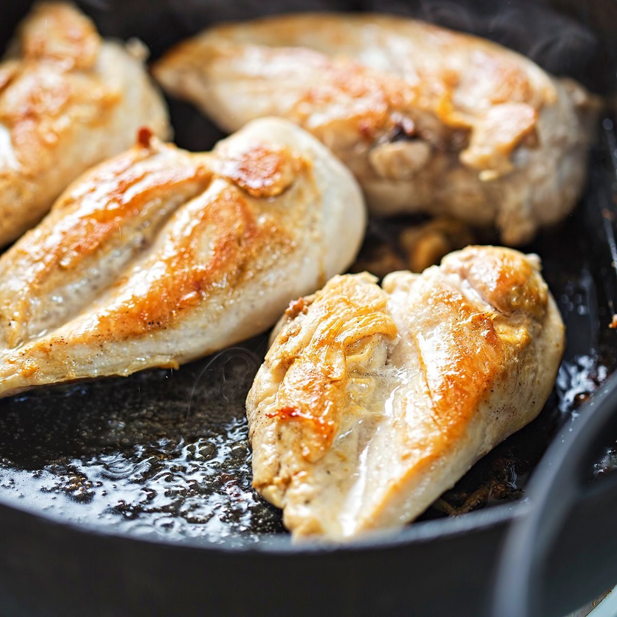 Fried chicken breasts on vegetable oil, iron cast pan