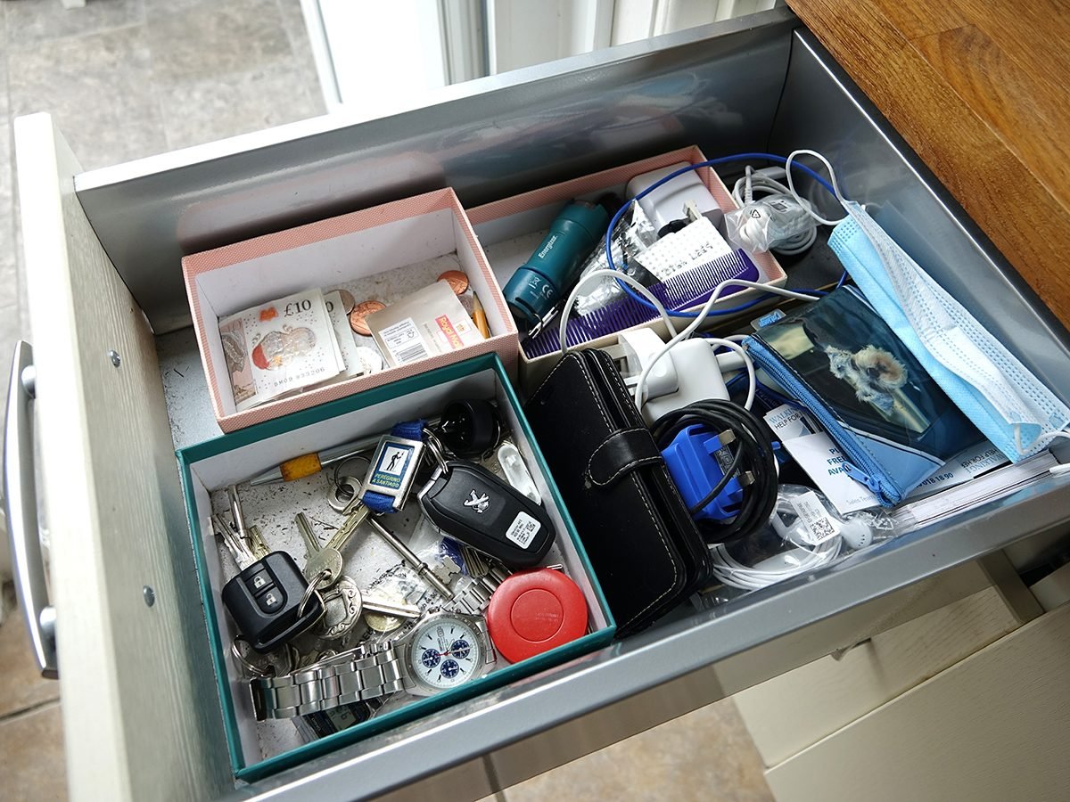 Dartmoor, England. June 2020. Kitchen drawer with essential items. Car keys, mobile phone, cash and notes, postage stamps. Purse. Phone chargers. Face mask. tape measure, House keys. In various boxes.