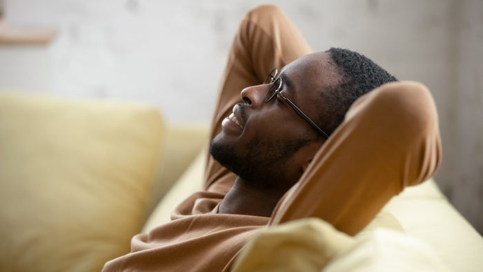 Signs you need new glasses - man in glasses sit relax on cozy couch lean hands over head taking nap in living room,