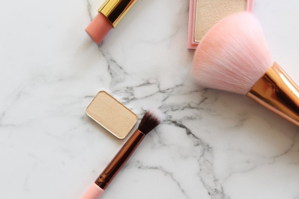 Gold and pink makeup objects against white marble copy space.