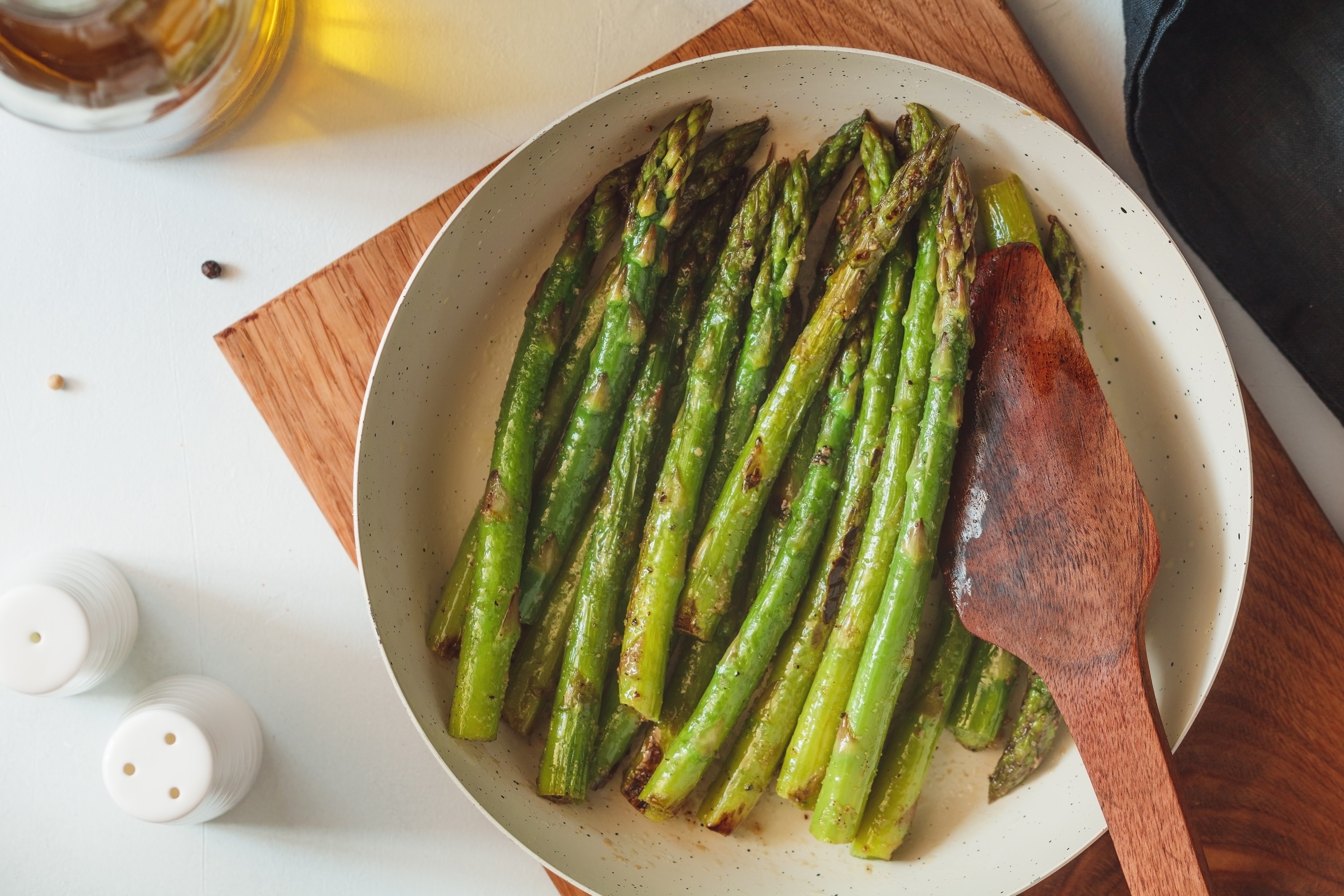 Top view on roasted asparagus in a white pan on a kitchen table. Modern style, vegetarian food.