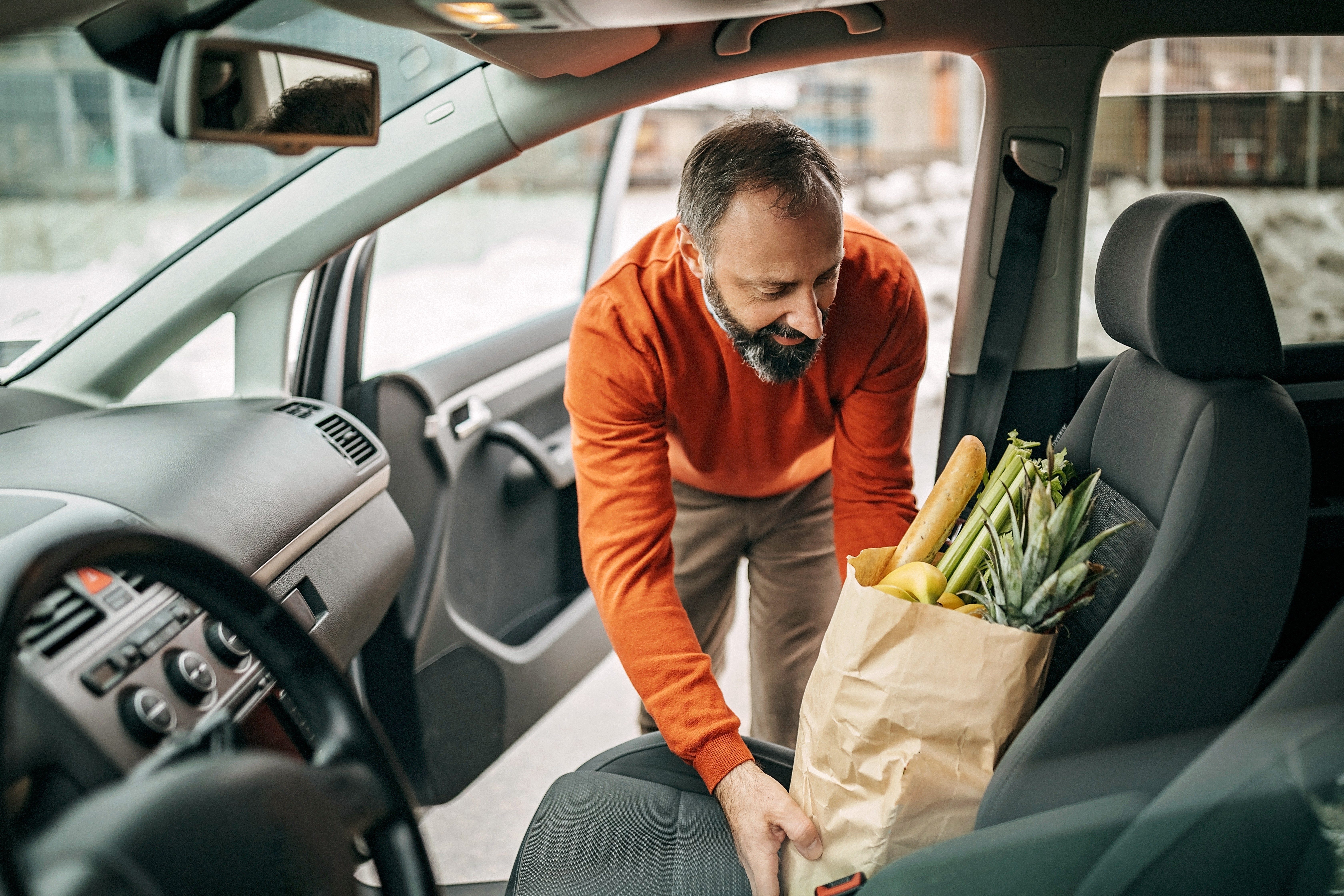 man placing paper bag full of groceries on the passenger side front seat