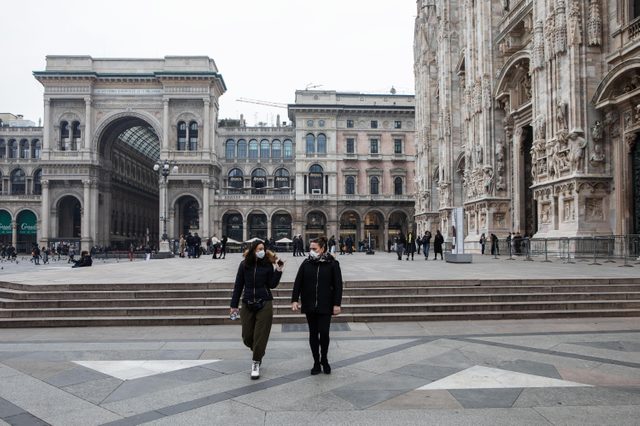 Two women, both wearing a respiratory mask, walk in Piazza del Duomo on February 25, 2020 in Milan, Italy.