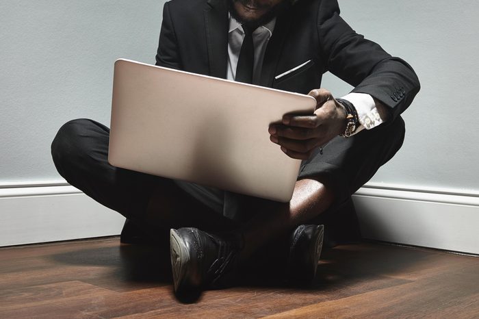 business man sitting on the floor in the corner with laptop