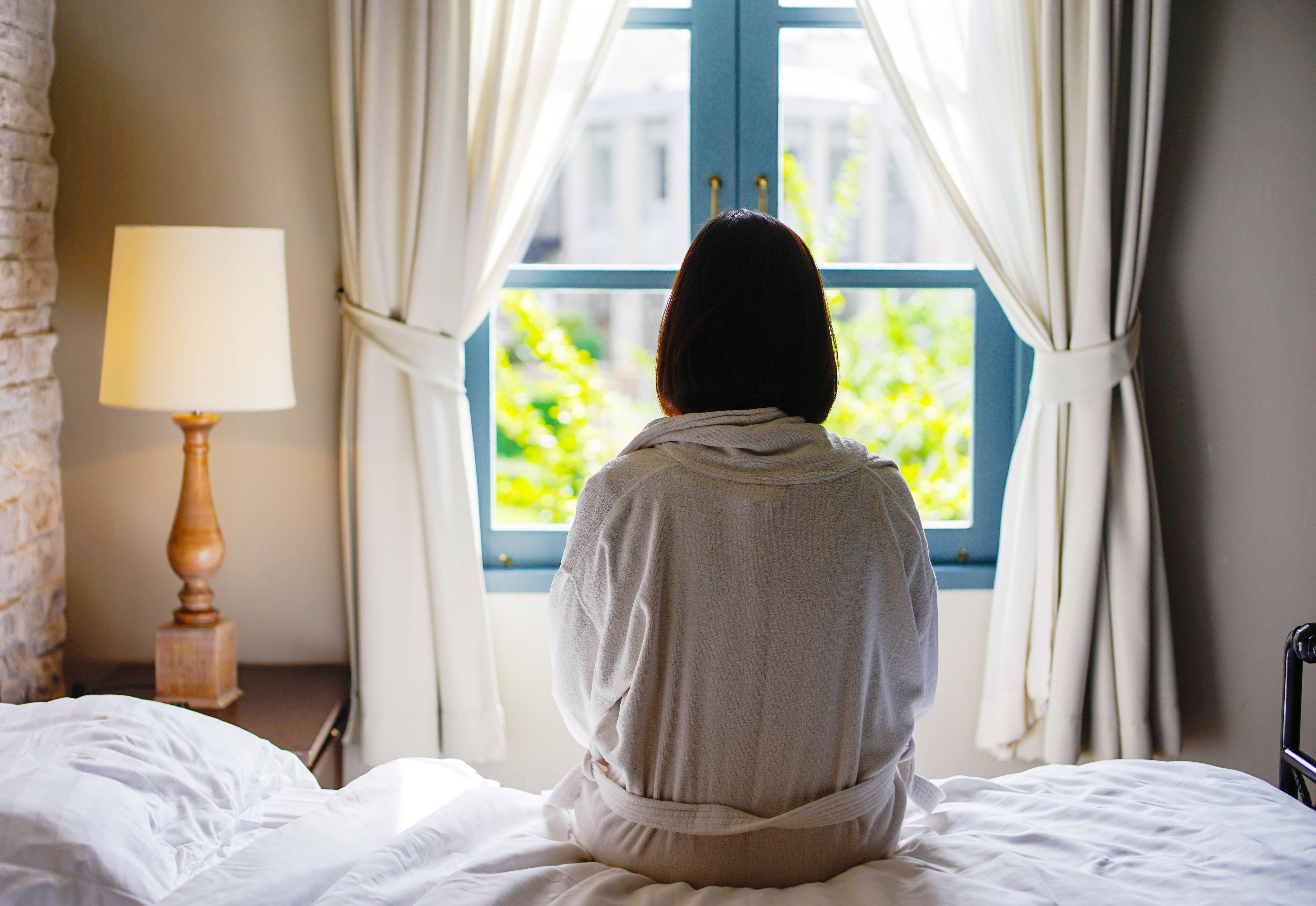 woman sits on the edge of the bed looking out window