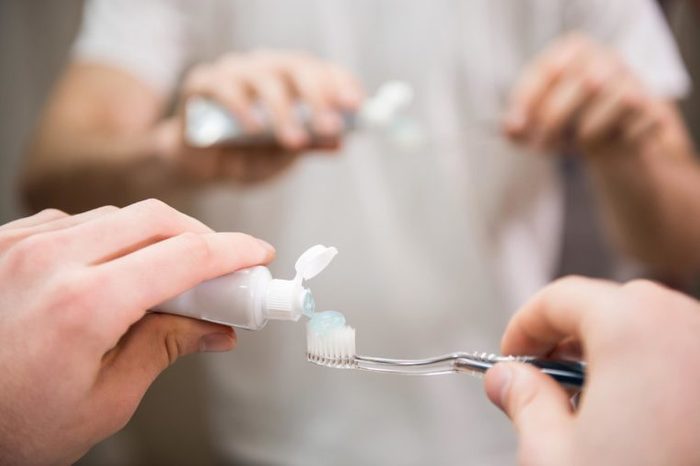 Dental health care clinic. Close-up of young man's hands is holding a toothbrush and placing toothpaste on it.
